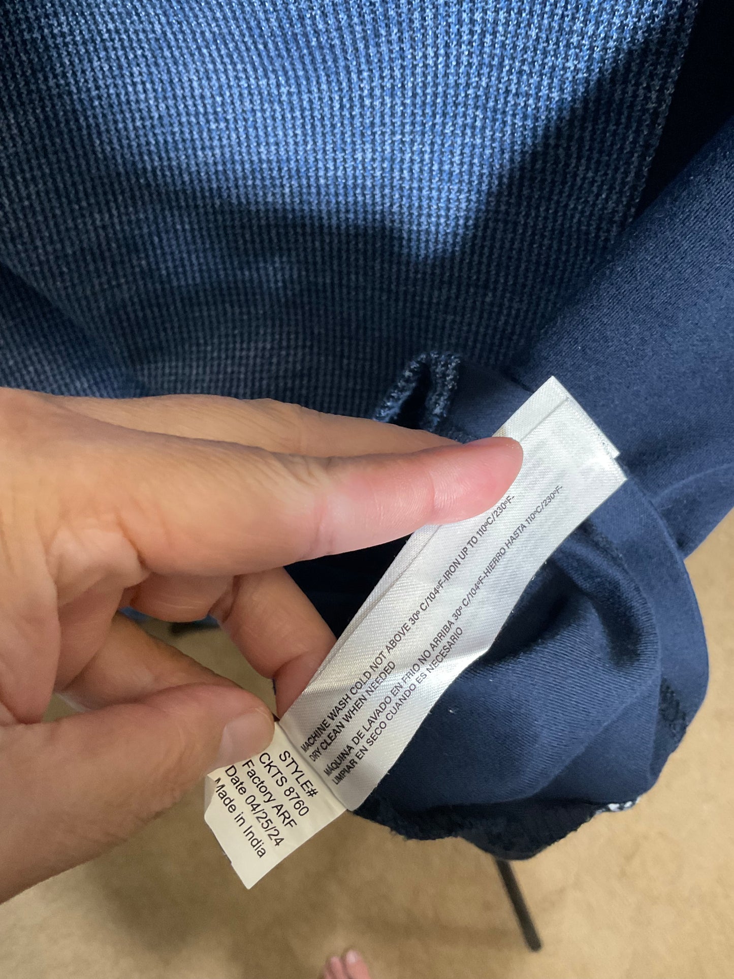 A close-up of a person's hand holding a white care label attached to a navy blue knit garment, showing the brand 'BONSAI' and other care instructions.
