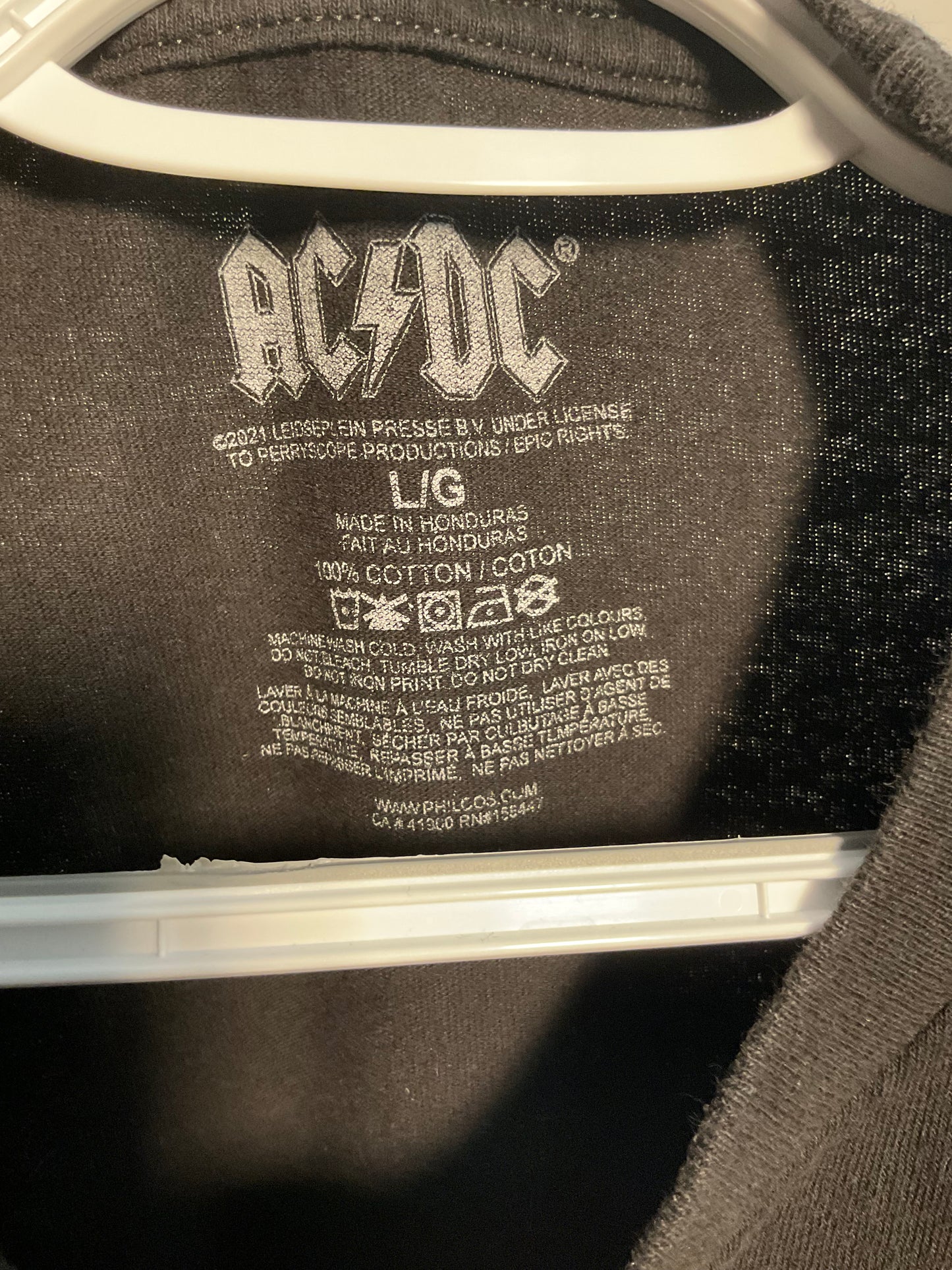 Close-up of the inside neck label of a dark gray or black AC/DC t-shirt on a white hanger, showing the AC/DC logo and garment details.