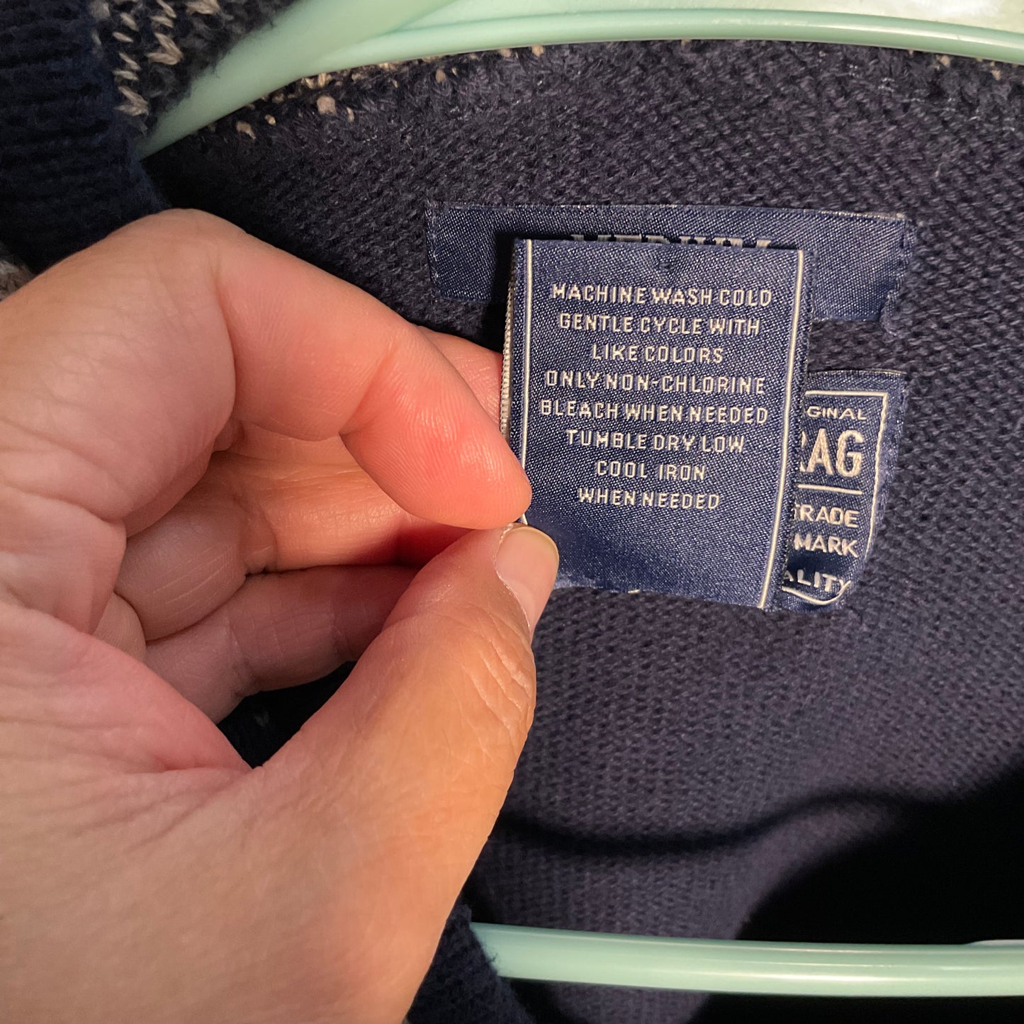 A close-up of a person's hand holding open a navy blue knit sweater's inner label, showing care instructions and a size tag.
