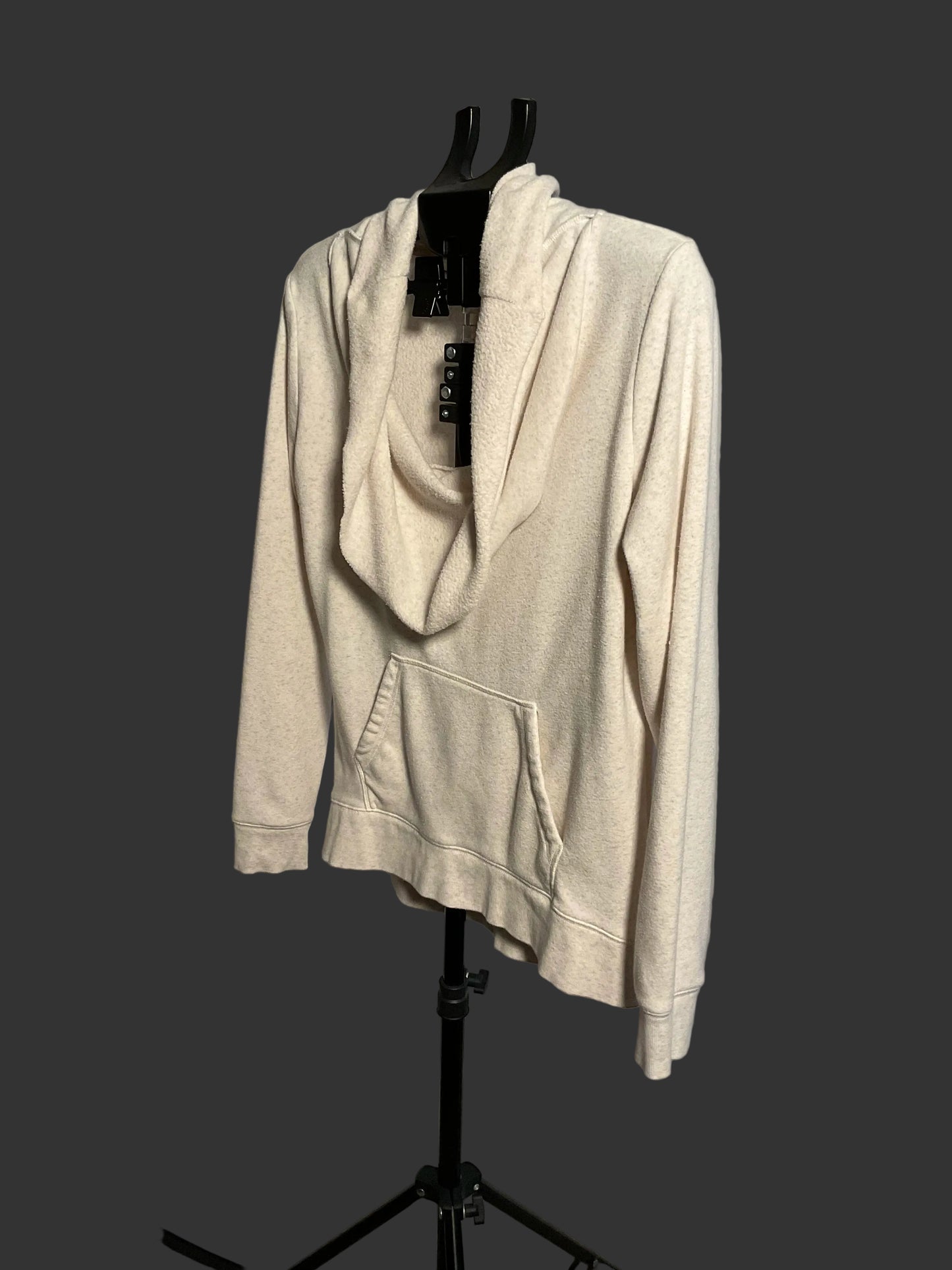 A cream-colored cowl neck pullover hoodie with a front kangaroo pocket, displayed on a black hanger stand against a circular studio backdrop.