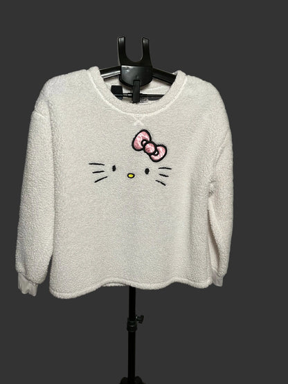 A white fuzzy long-sleeve sweatshirt featuring an embroidered Hello Kitty face and bow on the front, hanging on a black hanger against a gray studio backdrop.