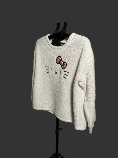 A white textured fleece long-sleeve sweater featuring an embroidered Hello Kitty face and bow on the front, displayed on a black hanger stand against a circular studio backdrop.