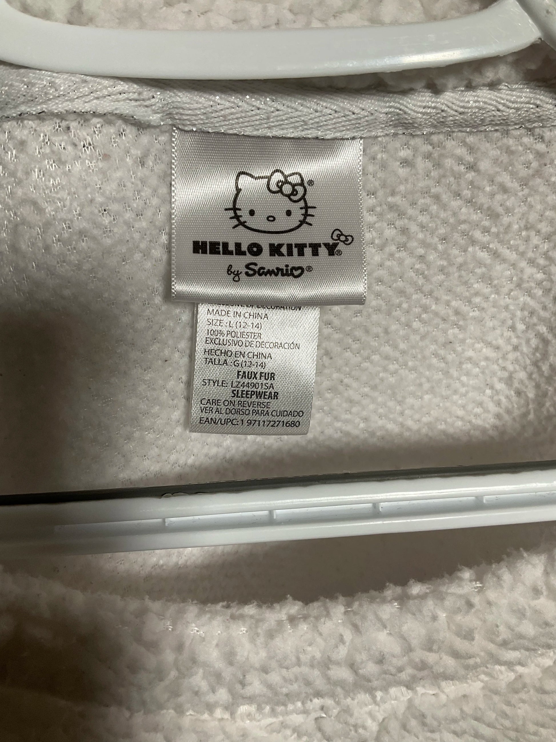 Close-up of a Hello Kitty by Sanrio fabric tag sewn onto a white textured garment, with a white plastic hanger visible at the top.