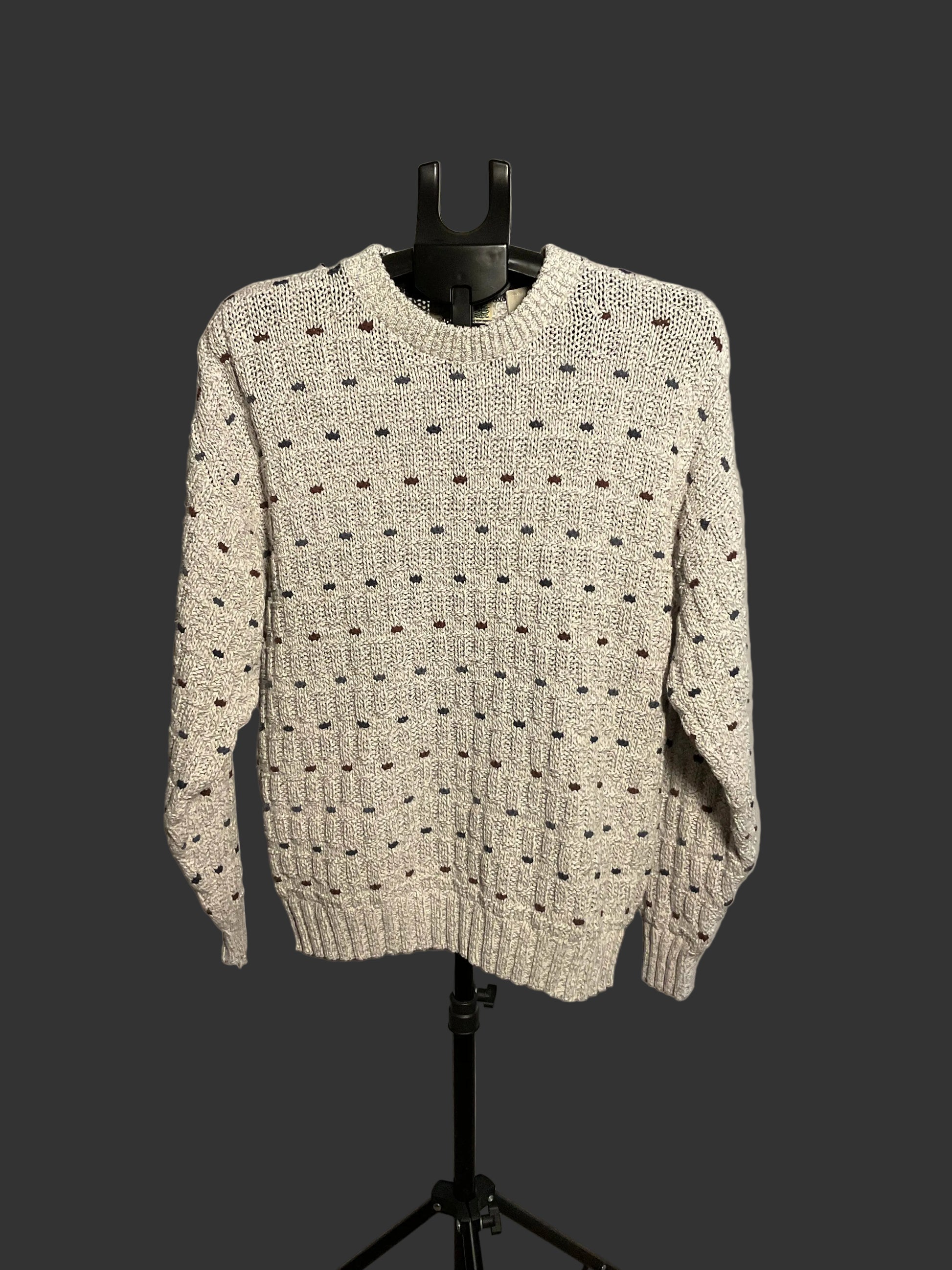 A cream-colored knit sweater with a textured dotted pattern, displayed on a black hanger stand against a white circular backdrop.