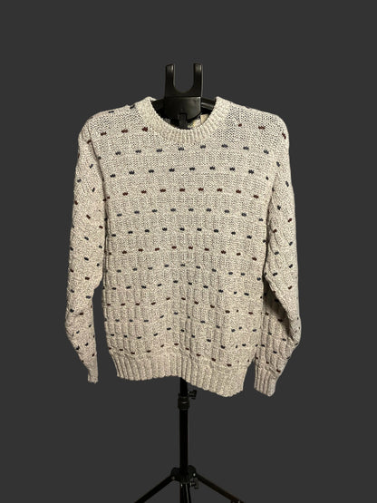 A cream-colored knit sweater with a textured dotted pattern, displayed on a black hanger stand against a white circular backdrop.
