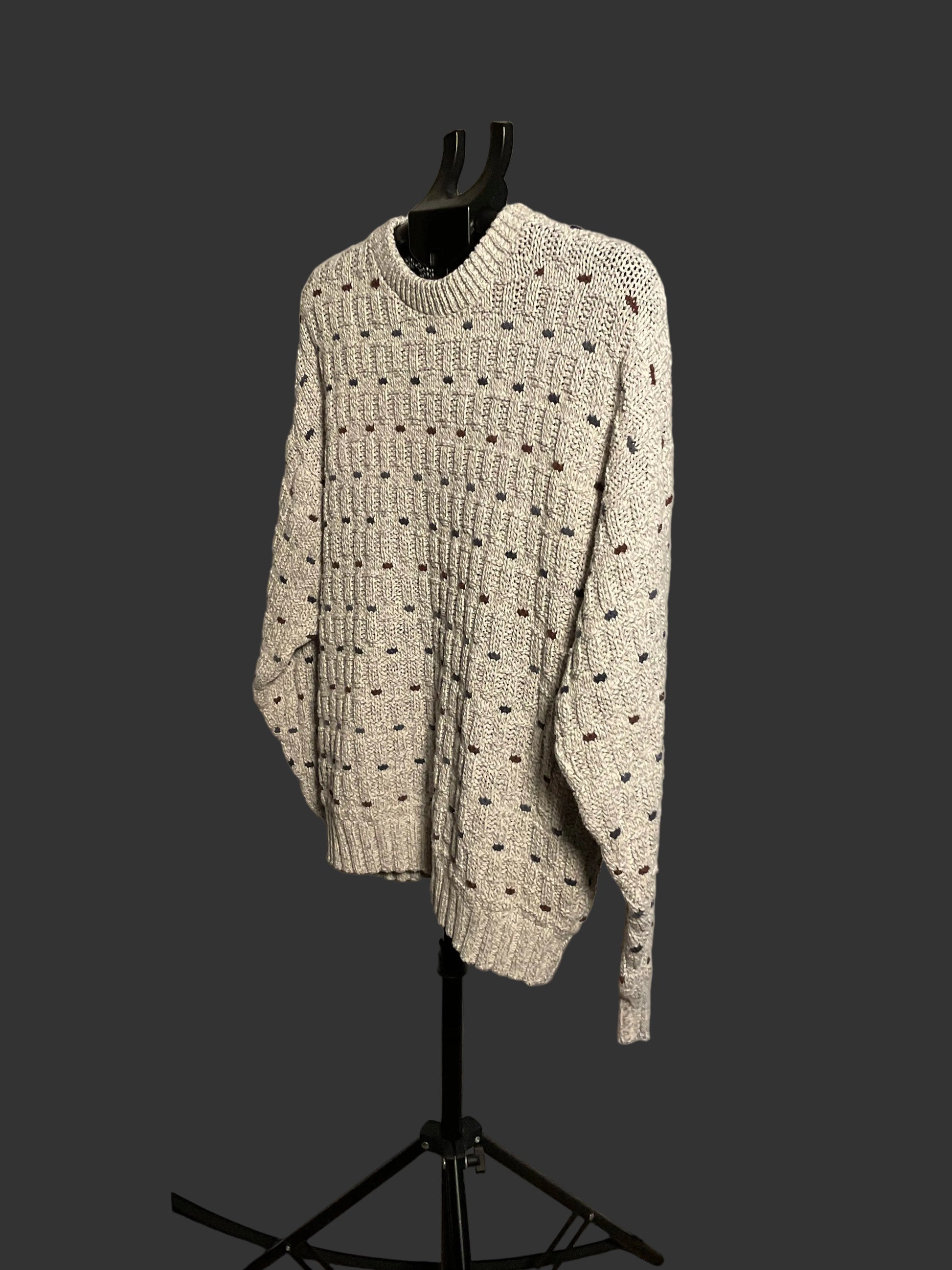 A cream-colored knit sweater with a textured dotted pattern, displayed on a black mannequin torso on a stand in front of a circular studio backdrop.