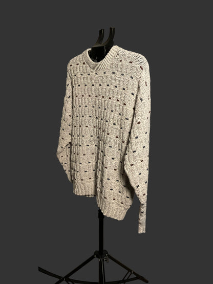 A cream-colored knit sweater with a textured dotted pattern, displayed on a black mannequin torso on a stand in front of a circular studio backdrop.