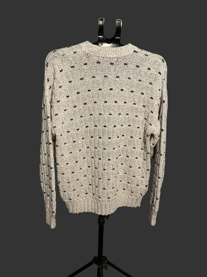 A cream-colored knit sweater with a black dotted pattern, displayed on a black mannequin stand against a light gray backdrop.