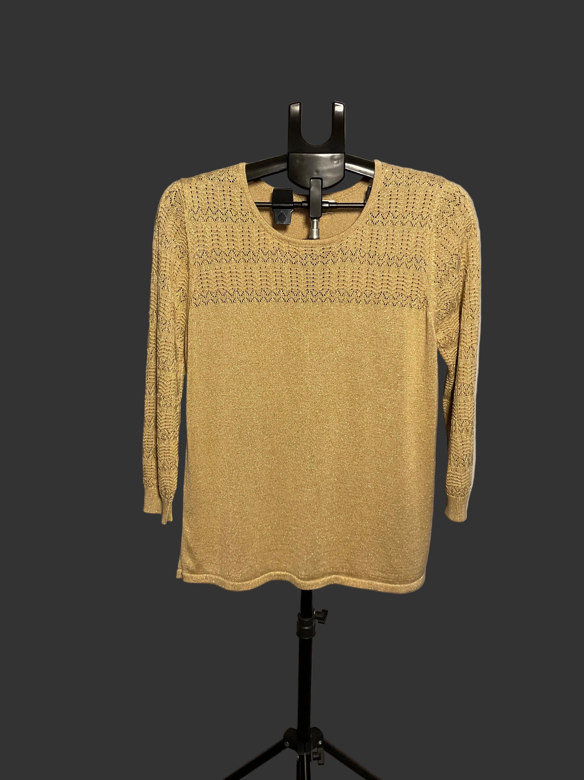 A mustard yellow knit sweater with a textured geometric pattern across the chest and shoulders, displayed on a black hanger stand against a white circular studio backdrop.