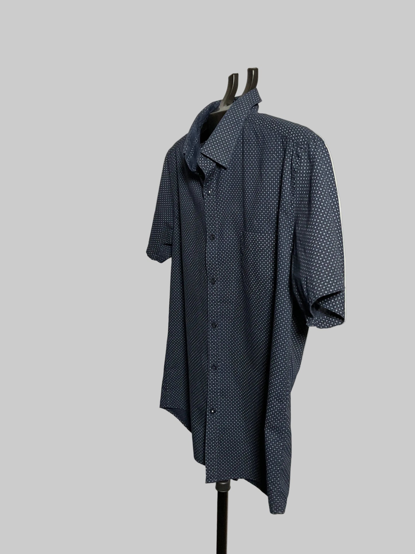 A dark blue short-sleeve button-up shirt with a small white geometric pattern, displayed on a black hanger stand against a white studio backdrop.