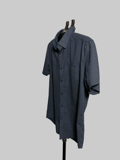 A dark blue short-sleeve button-up shirt with a small white geometric pattern, displayed on a black hanger stand against a white studio backdrop.