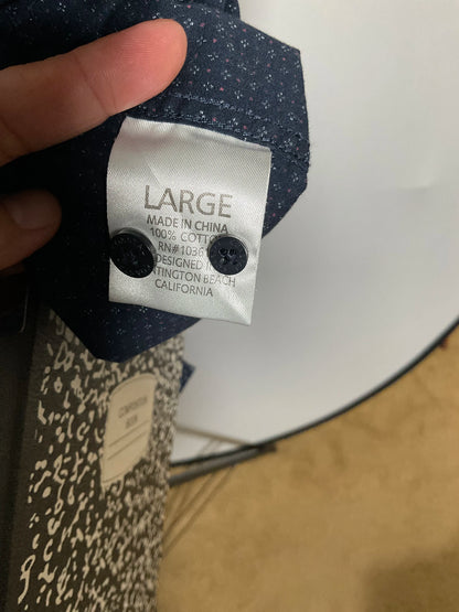 A close-up of a navy blue patterned shirt fabric held by a hand, showing a white sewn-in size label that reads LARGE with manufacturing details.