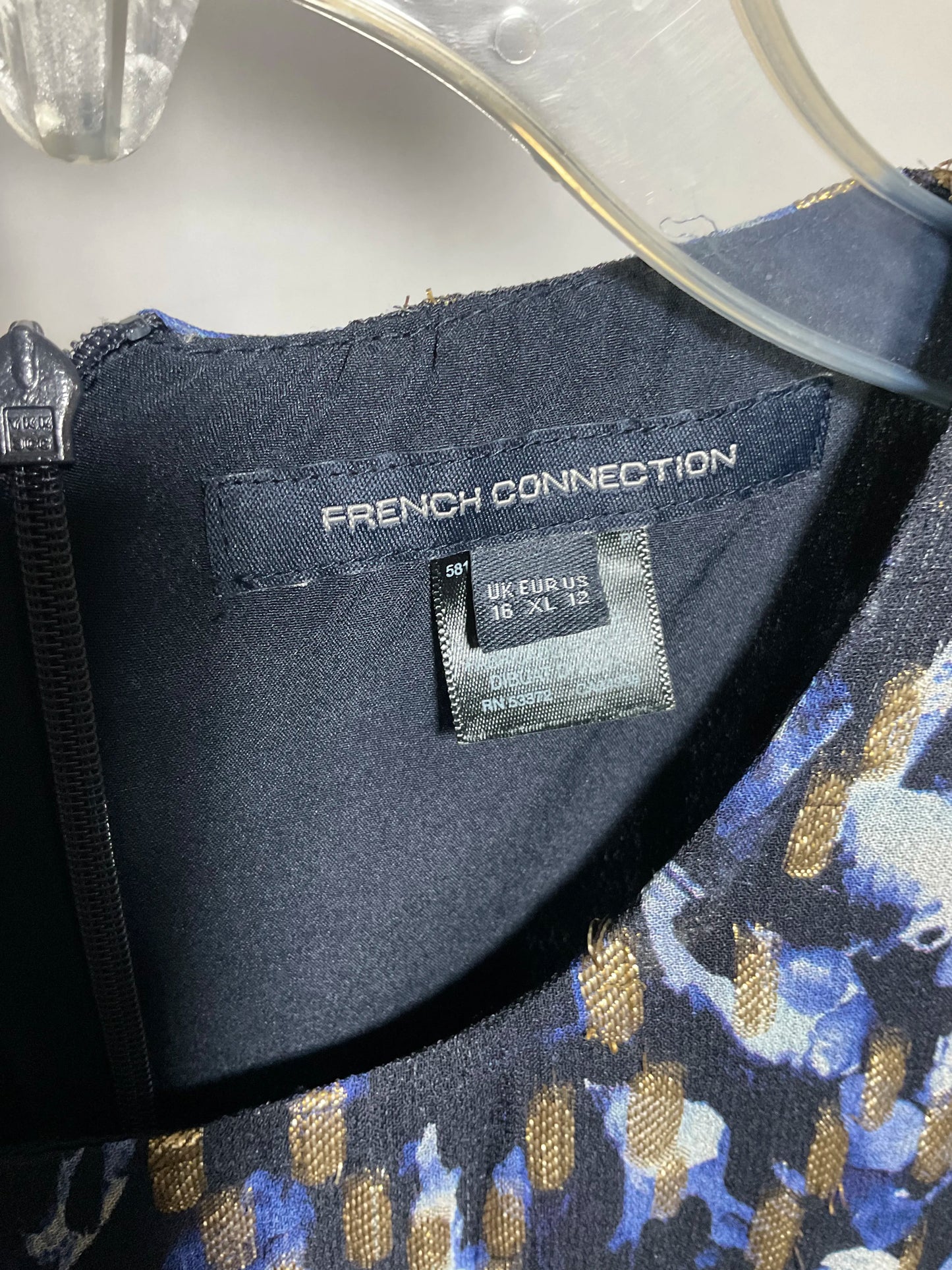 Close-up of the inside neckline of a French Connection garment, showing the brand label and a size tag reading 18 XL, with a blue, black, and gold patterned fabric visible.