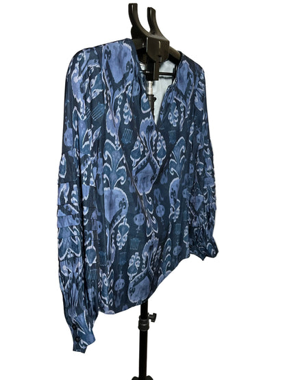 A long-sleeve blue patterned blouse displayed on a black hanger stand against a plain off-white wall.