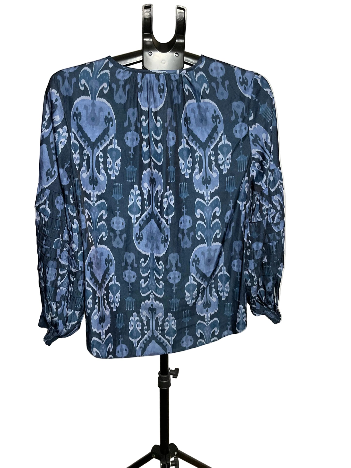 A long-sleeve blouse with a blue and white ikat-style pattern, displayed on a black hanger stand against a white studio backdrop.
