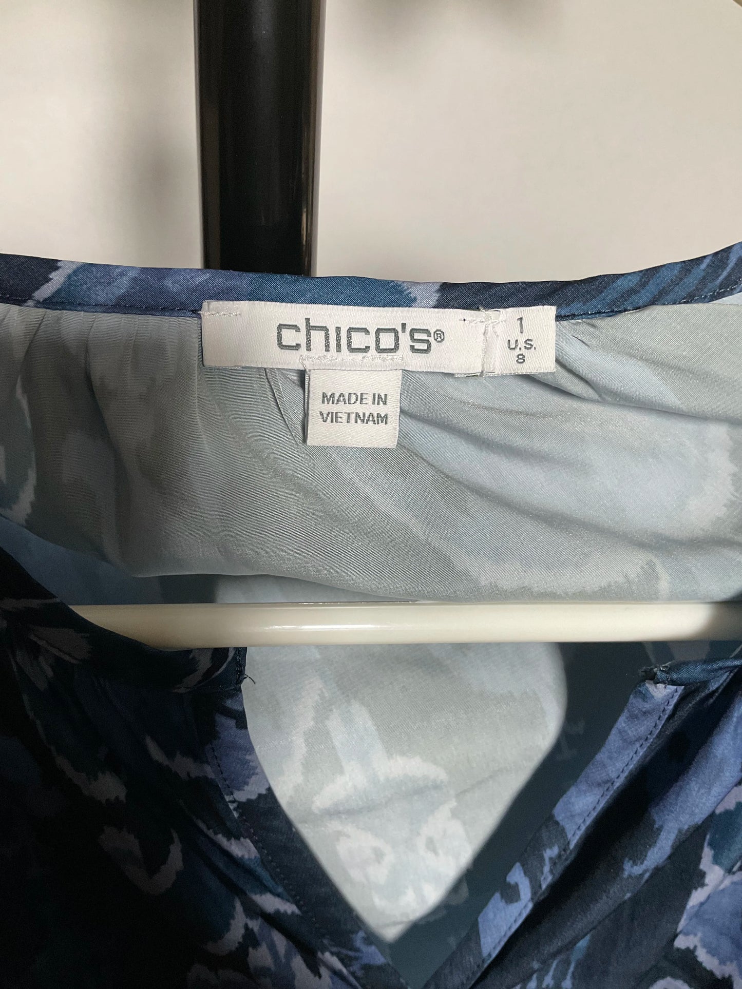 Close-up of a blue patterned garment hanging on a white hanger, showing the brand label 'chico's' and size information.