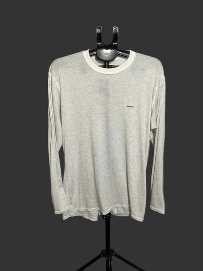 A light gray long-sleeve crewneck shirt with a small black logo on the left chest, displayed on a black hanger stand against a dark gray background.