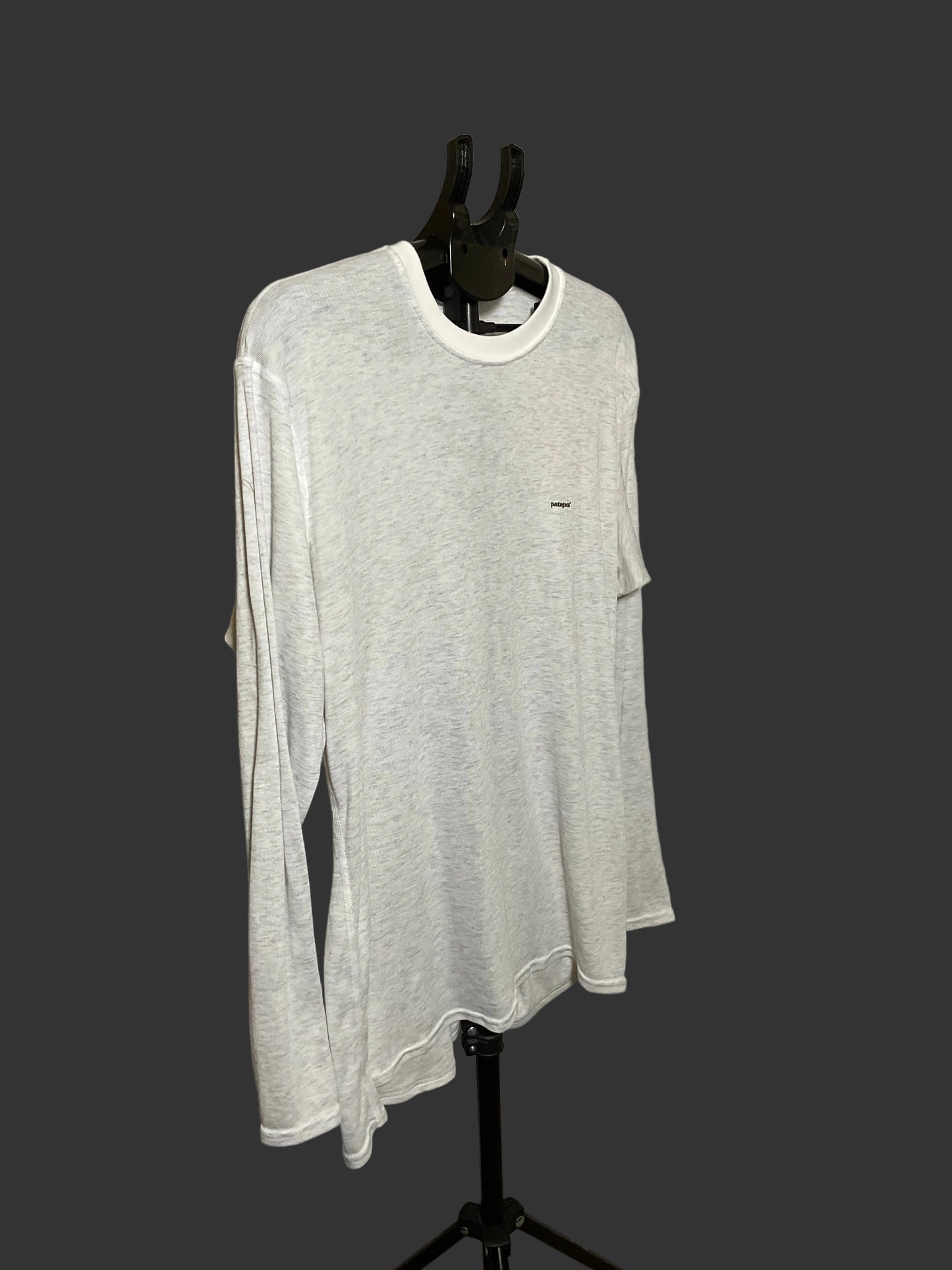 A light gray heather long-sleeve t-shirt with a white crew neck collar, displayed on a black mannequin torso against a dark gray background.