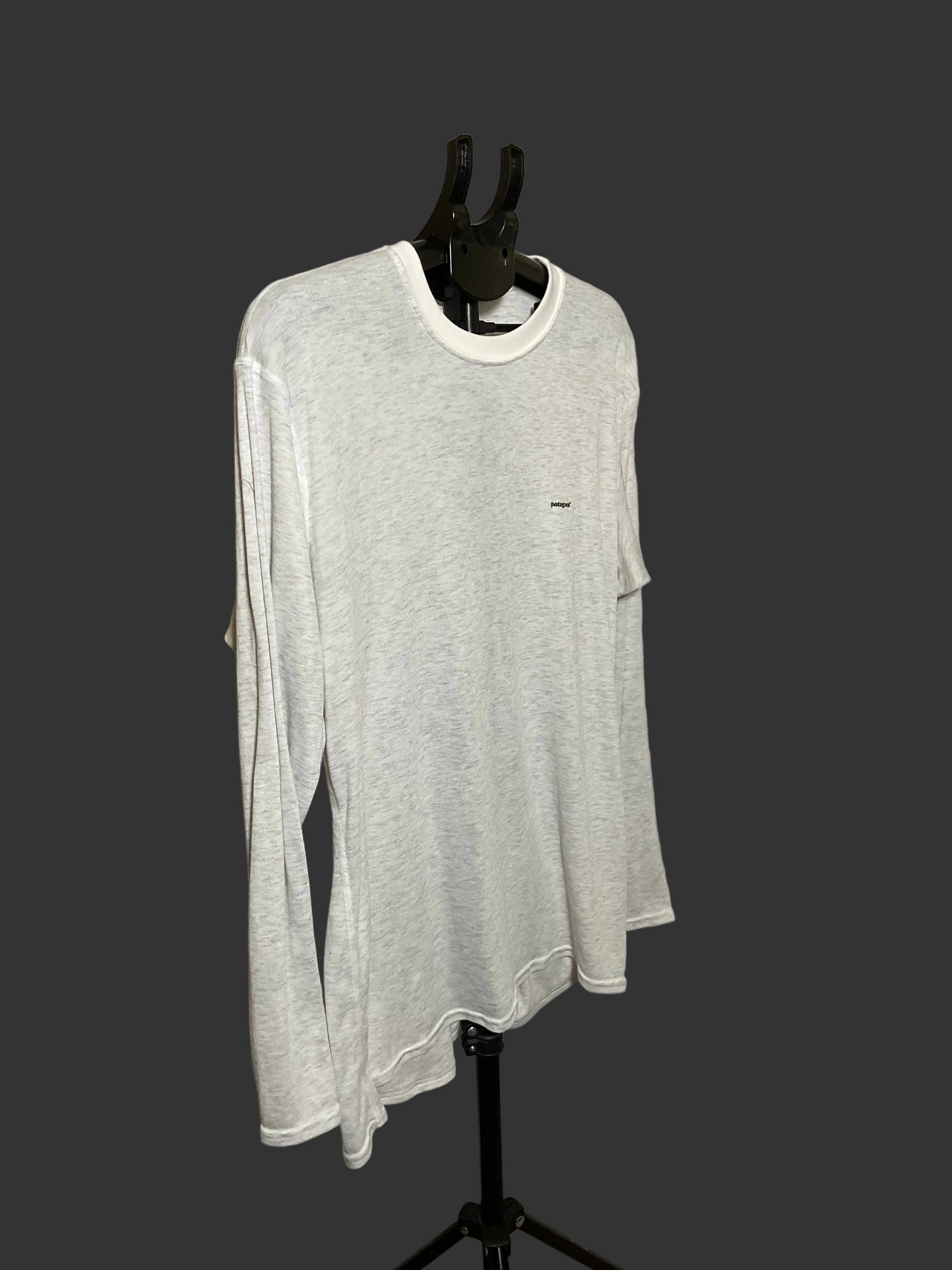 A light gray heather long-sleeve t-shirt with a white crew neck collar, displayed on a black mannequin torso against a dark gray background.