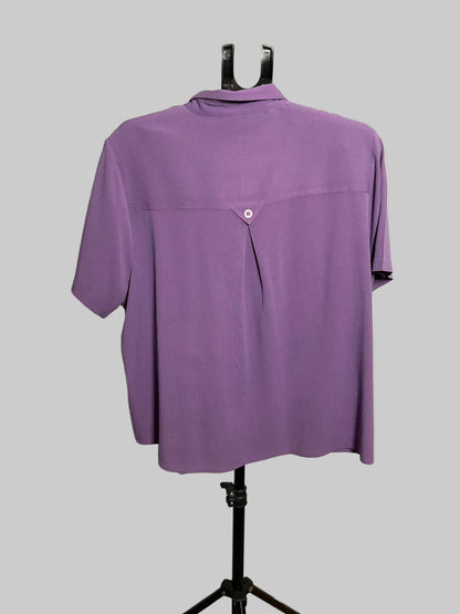 A purple short-sleeve button-up shirt displayed on a black dress form stand against a plain off-white wall.