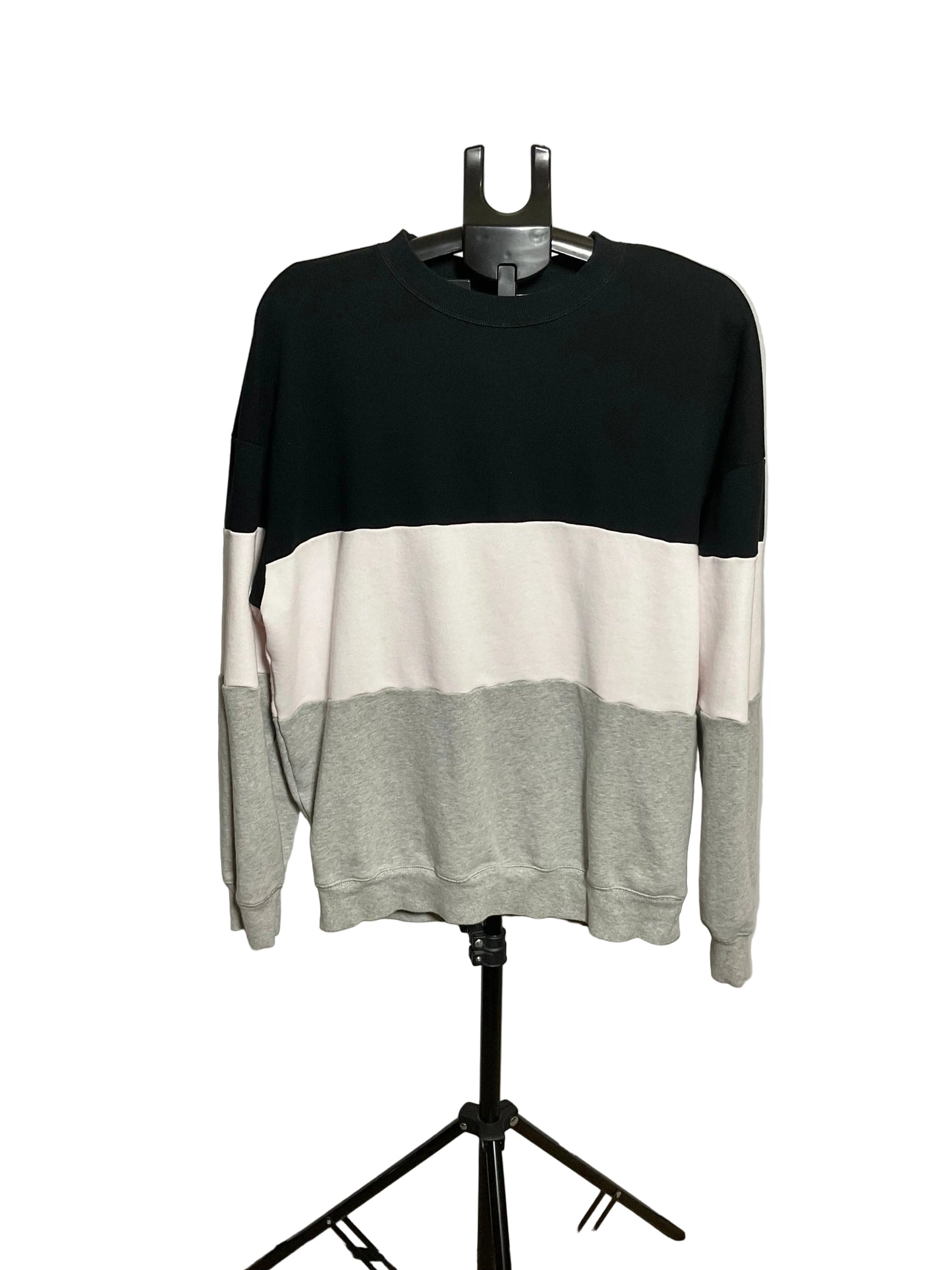 A crewneck sweatshirt with a three-block color design of black, off-white, and light gray, displayed on a black hanger stand against a white circular backdrop.