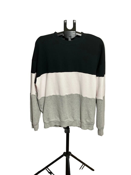 A crewneck sweatshirt with a three-block color design of black, off-white, and light gray, displayed on a black hanger stand against a white circular backdrop.