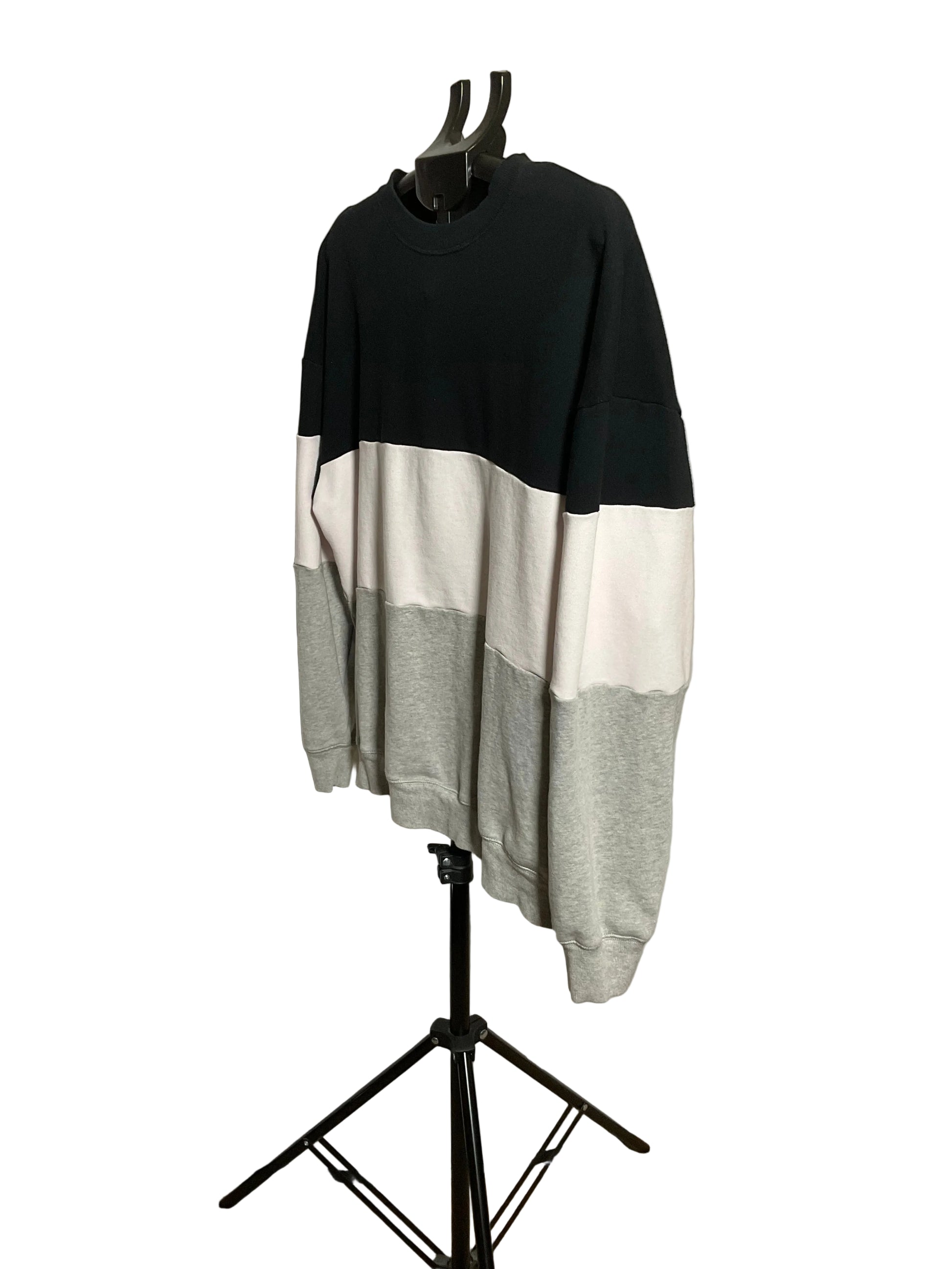 A color-block crewneck sweatshirt displayed on a black hanger stand against a white circular backdrop. The sweatshirt features three color blocks: black on the upper chest and shoulders, white across the middle, and light gray on the lower body and sleeves.