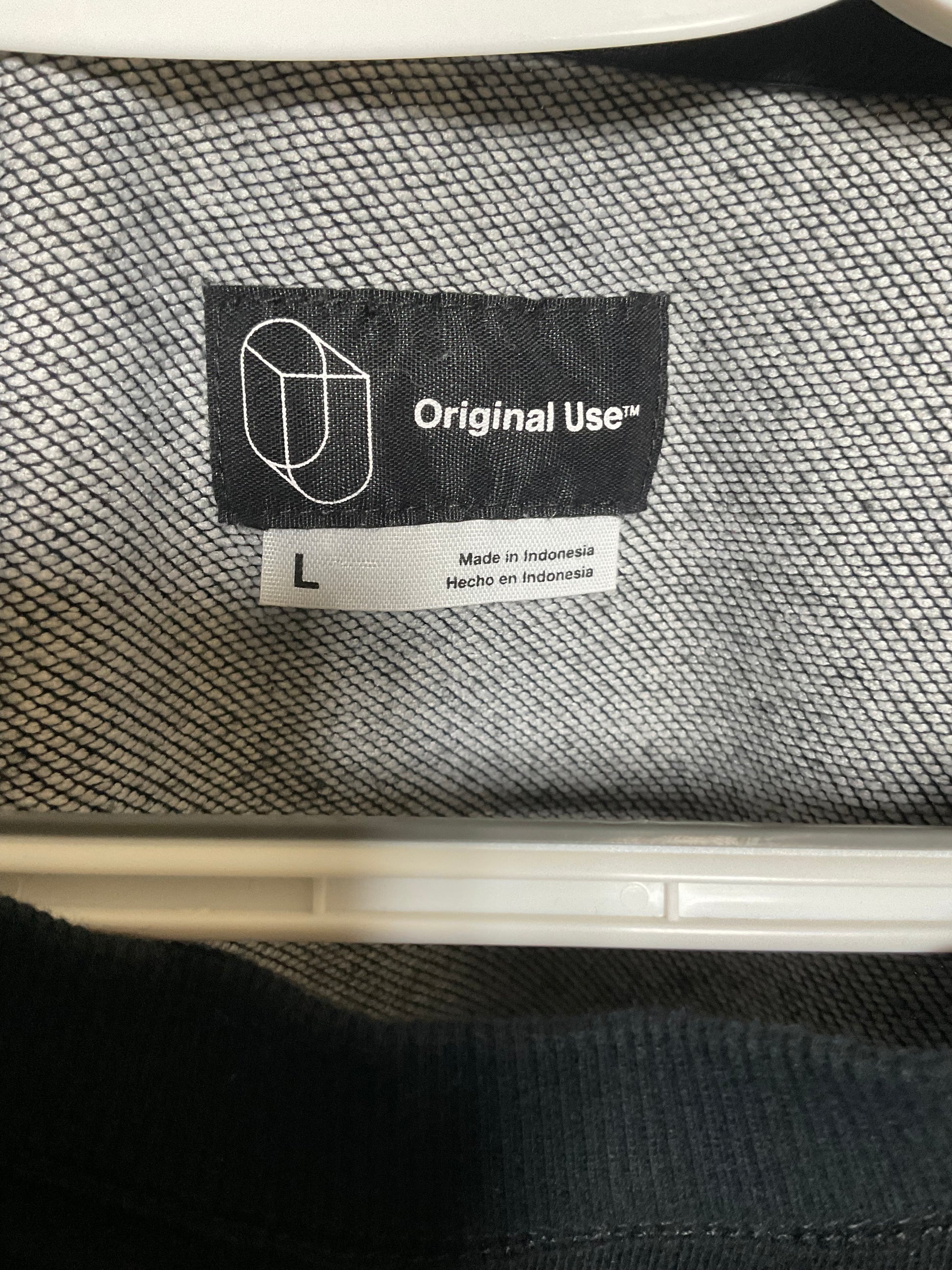 Close-up of a garment's interior neck label showing the brand 'Original Use' with size 'L' printed on a white tag, set against a gray textured knit fabric.
