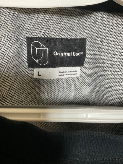 Close-up of a garment's interior neck label showing the brand 'Original Use' with size 'L' printed on a white tag, set against a gray textured knit fabric.