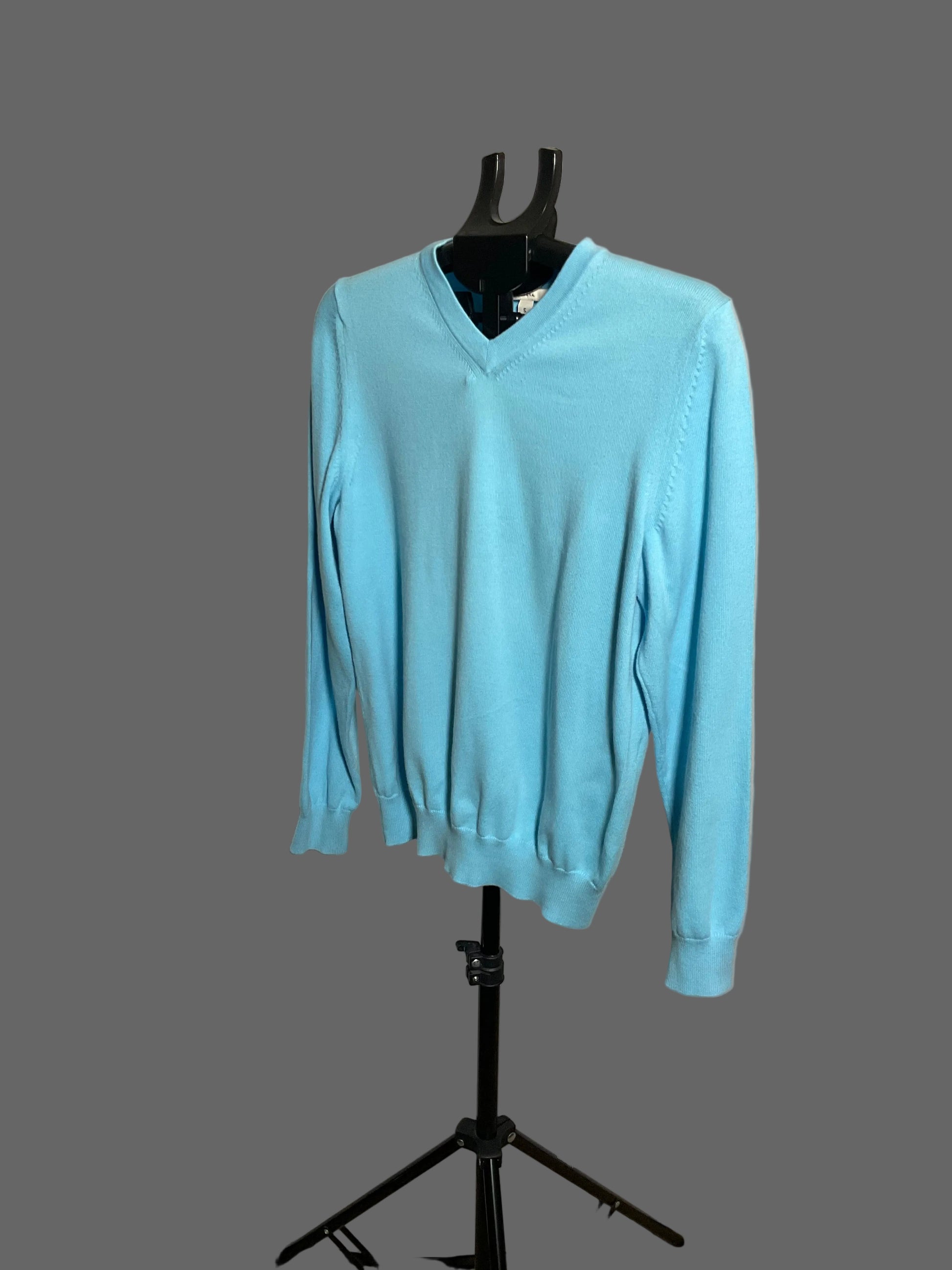 A light blue long-sleeve V-neck sweater displayed on a black dress form mannequin stand against a white circular studio backdrop.