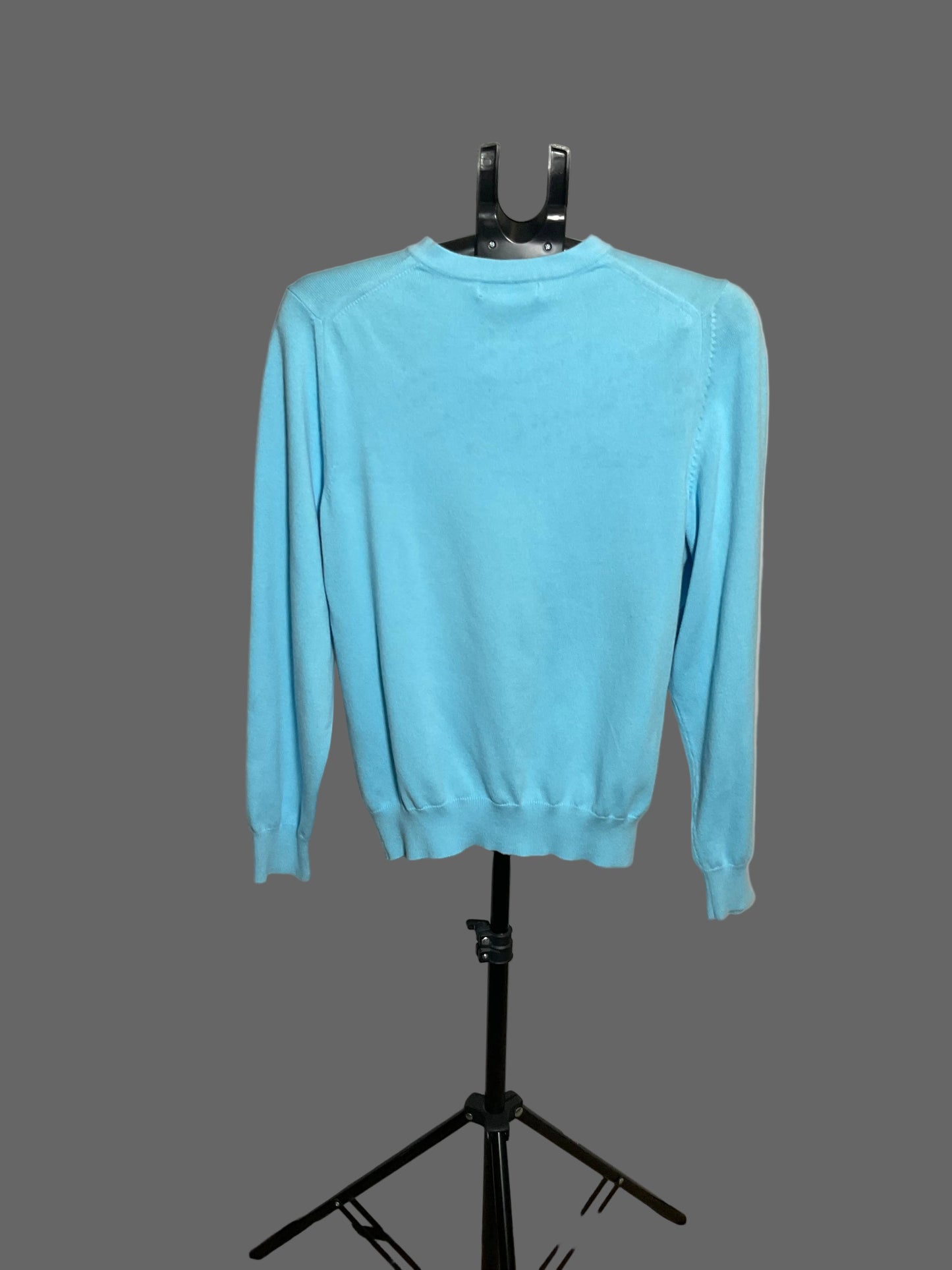 A light blue long-sleeve crewneck sweater displayed on a black hanger stand against a white circular studio backdrop.