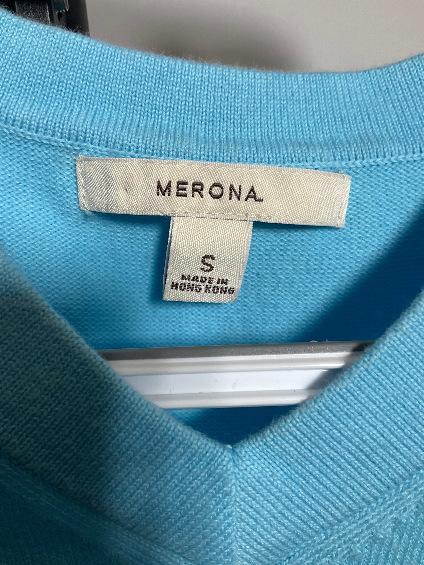 Close-up of a light blue knit sweater showing the interior neck label with the brand name MERONA and size S.