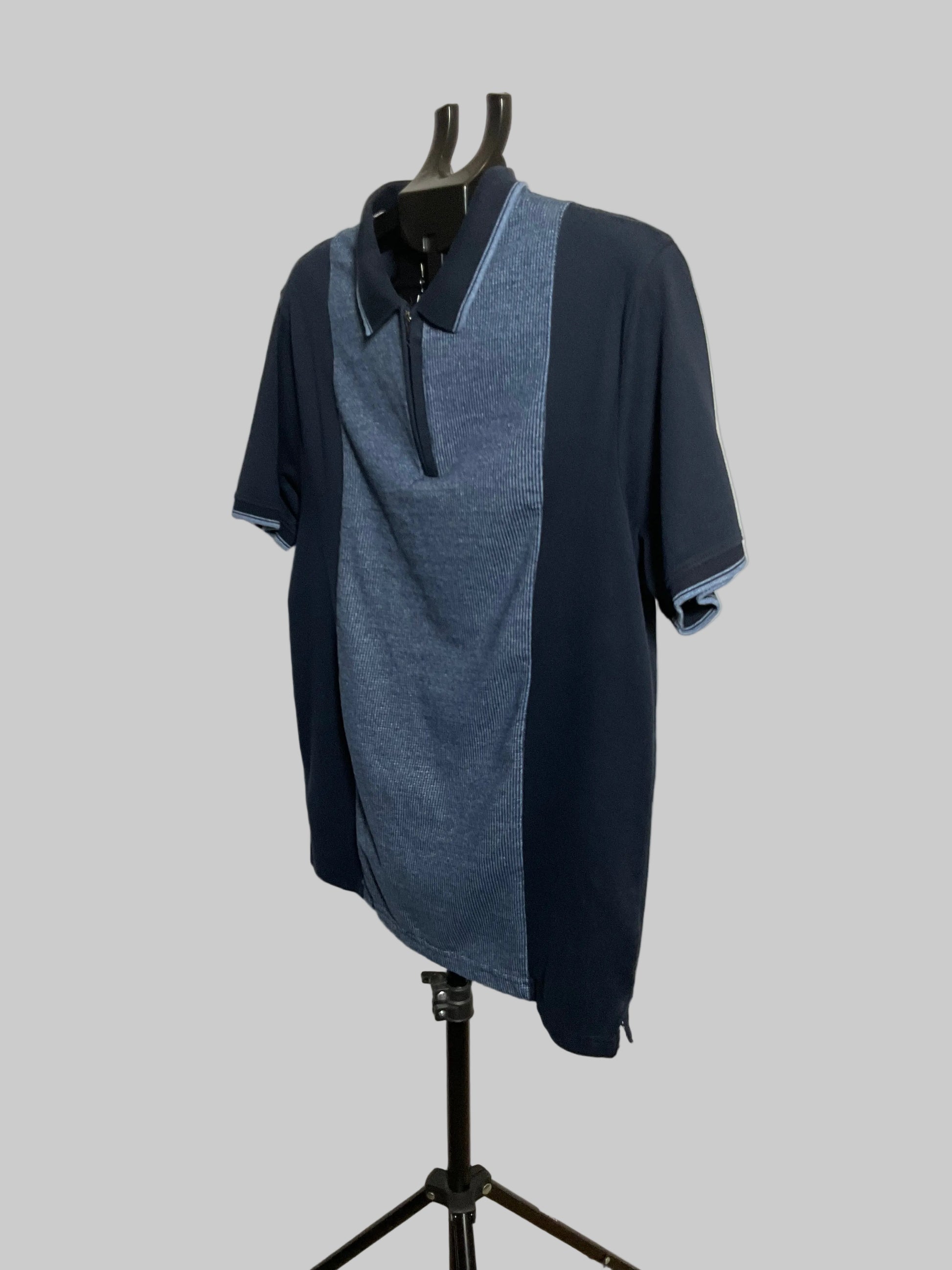 A short-sleeve polo shirt in navy and heathered blue, displayed on a black hanger stand against a plain off-white studio backdrop.