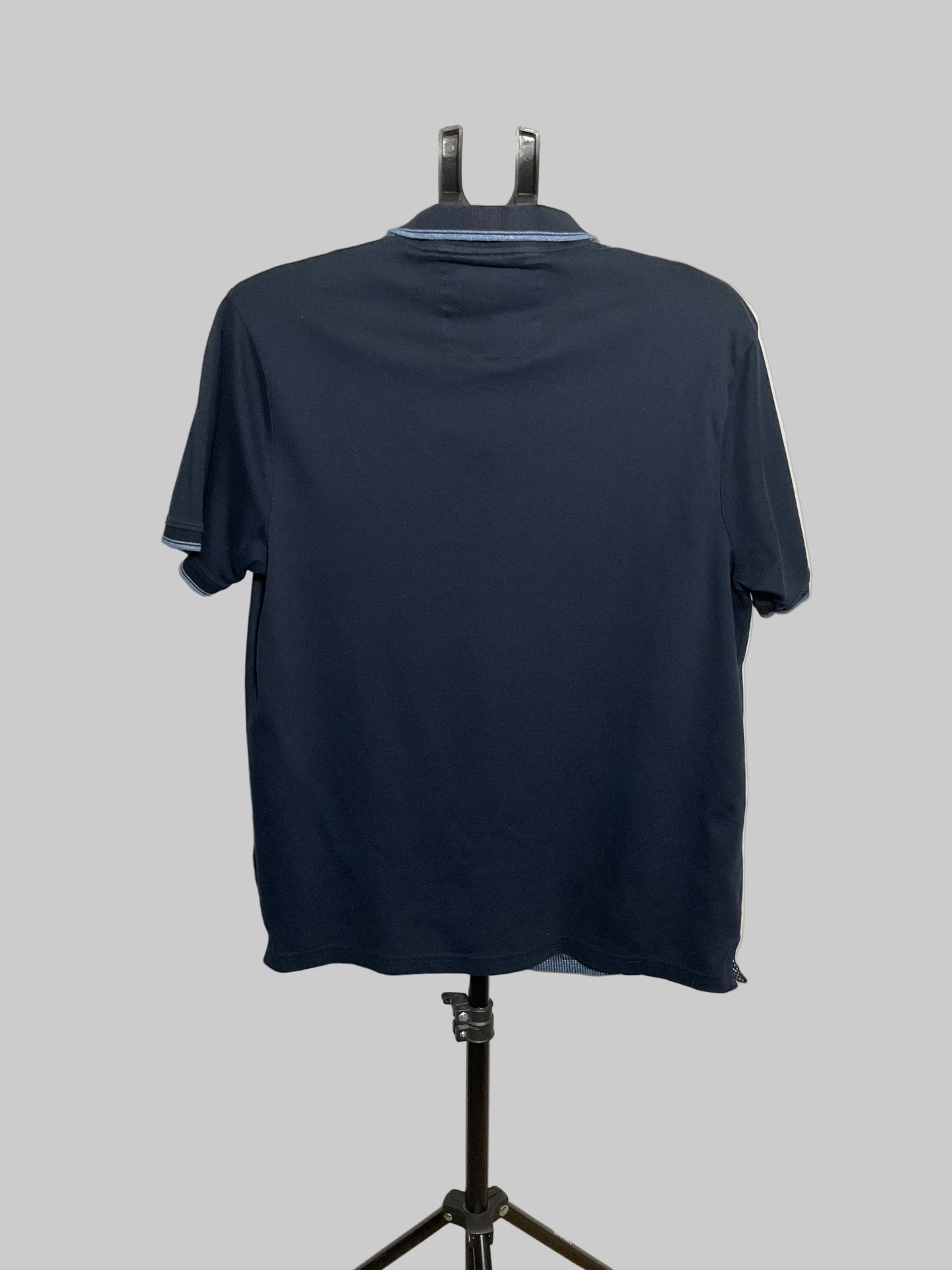 A dark navy blue short-sleeve polo shirt shown from the back, hanging on a black hanger mounted on a stand against a plain off-white wall.