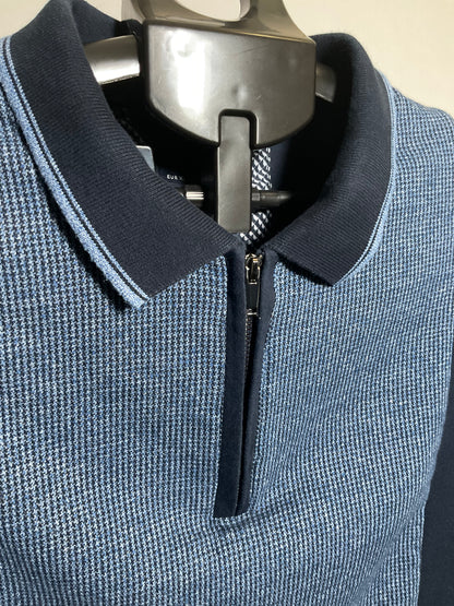A close-up of a men's blue and navy polo shirt with a textured knit pattern, featuring a half-zip collar and a silver metal hanger.