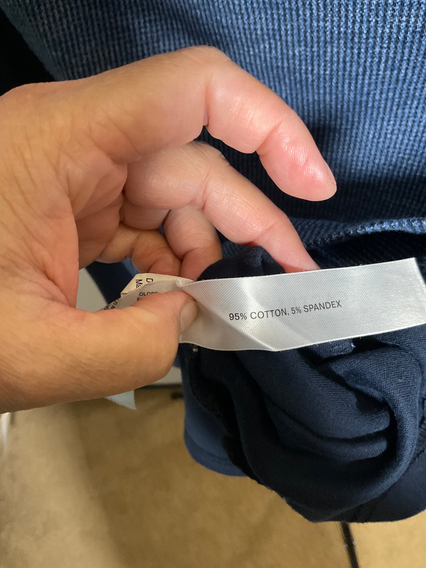 A close-up of a hand holding open a garment tag that reads '95% COTTON, 5% SPANDEX' against blue fabric.