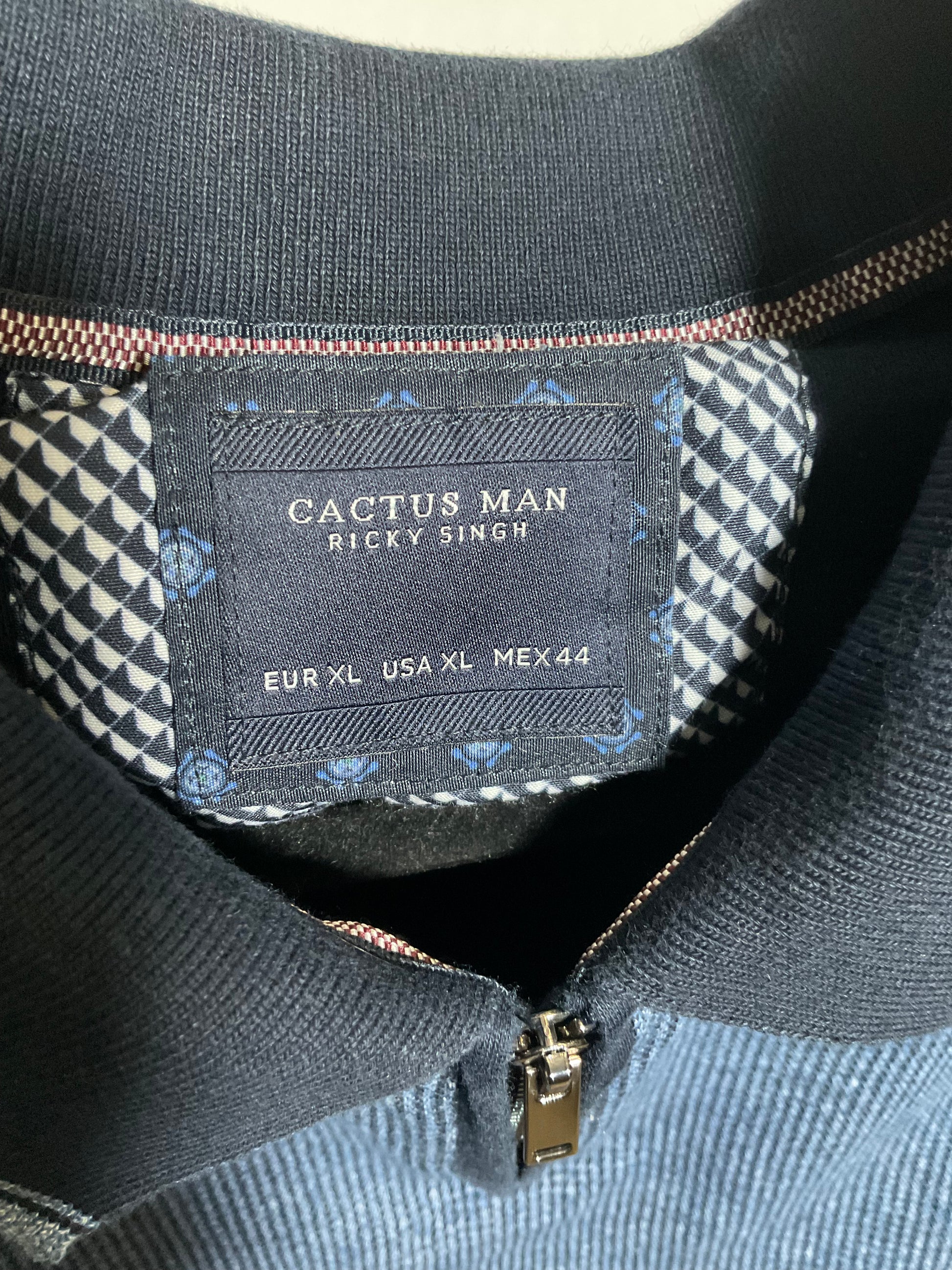 Close-up of the inner collar of a Cactus Man Ricky Singh zip-up sweater, showing the brand label, patterned lining, and dark ribbed collar.