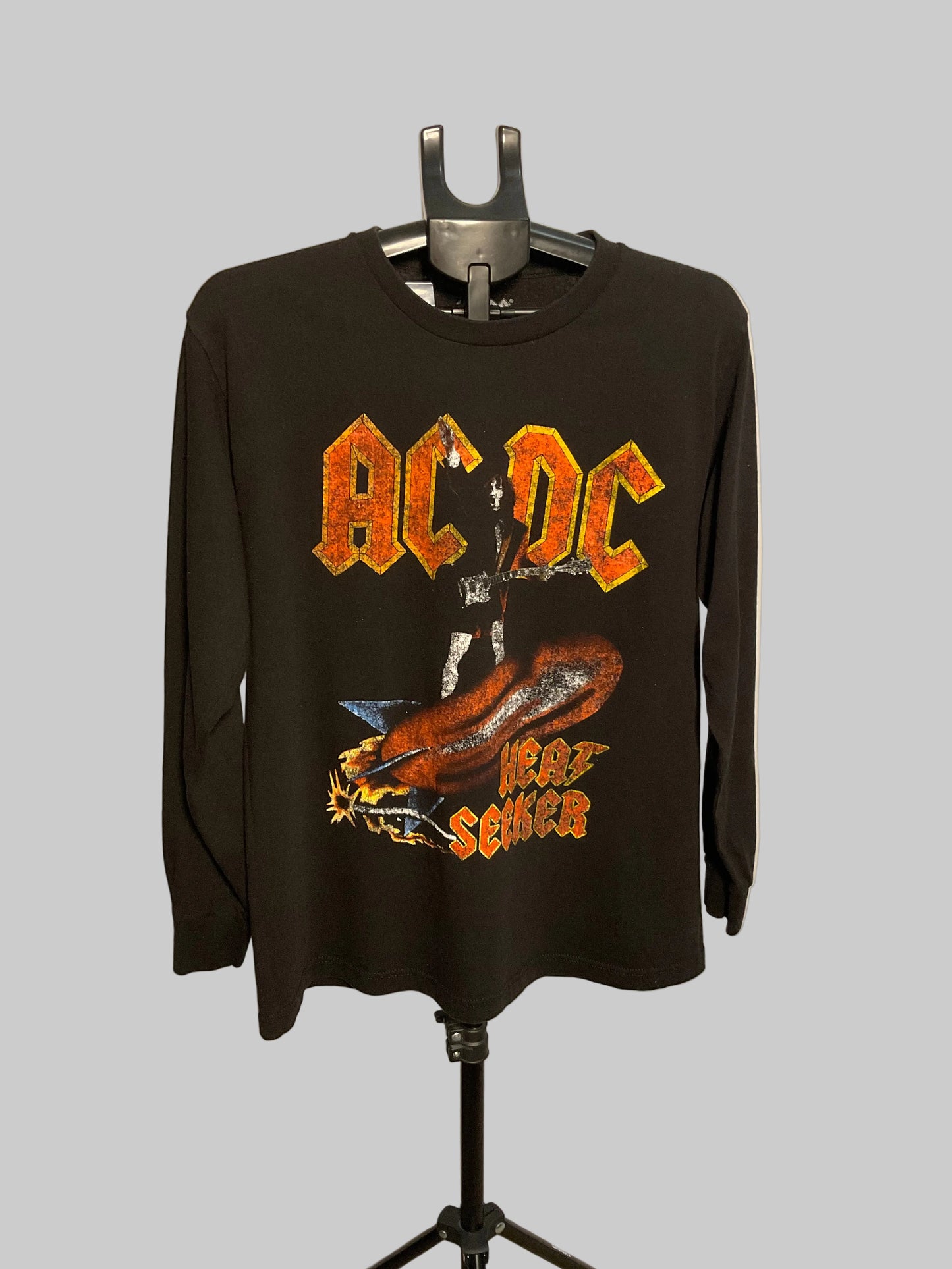 A black long-sleeve AC/DC 'Fear and Loathing in Seattle' graphic t-shirt hanging on a black hanger stand against a plain off-white wall.