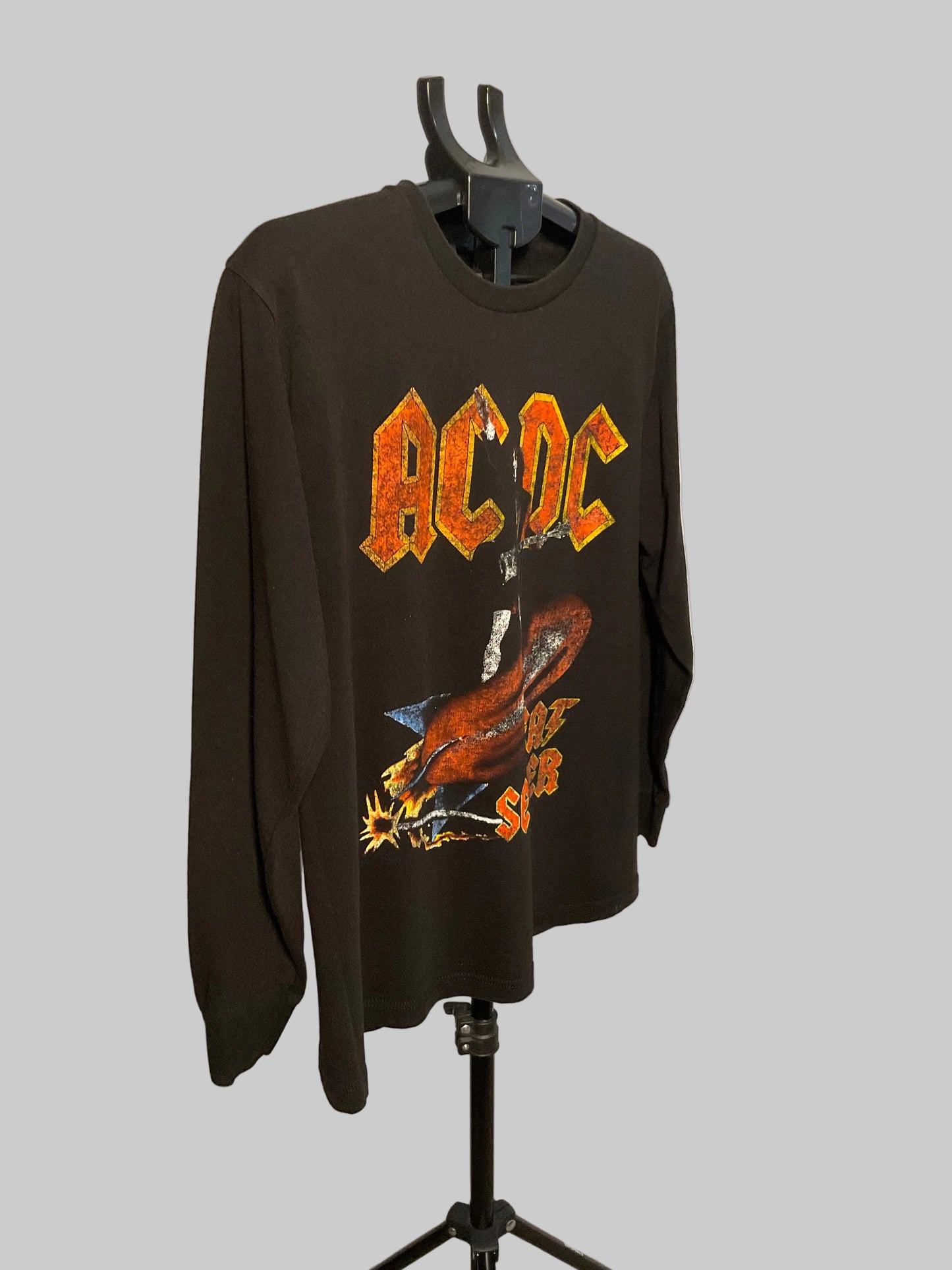 A black long-sleeve AC/DC 'Live at the Palace' graphic t-shirt displayed on a black hanger stand against a plain off-white wall.