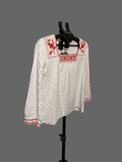 A white long-sleeve textured blouse with red embroidered details on the neckline and cuffs, displayed on a black hanger stand against a plain light gray backdrop.