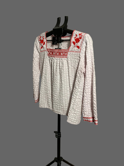 A white long-sleeve blouse with red floral embroidery and a smocked neckline, displayed on a black hanger stand against a plain light gray wall.