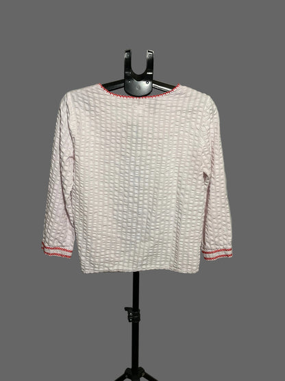 A light pink textured long-sleeve top with red trim on the collar and cuffs, displayed on a black hanger stand against a plain light gray background.