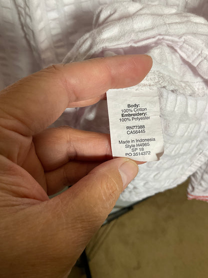 A close-up of a hand holding a white fabric care label that reads 'Body: 100% Cotton Embroidery: 100% Polyester Made in Indonesia Sija H4965' on a white textured garment.