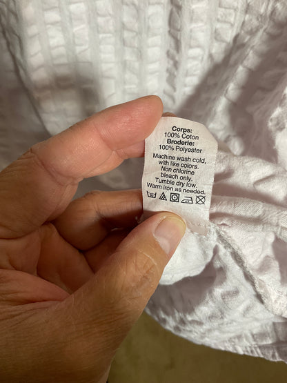 A close-up of a hand holding a white fabric care label with printed instructions, set against a textured white garment.
