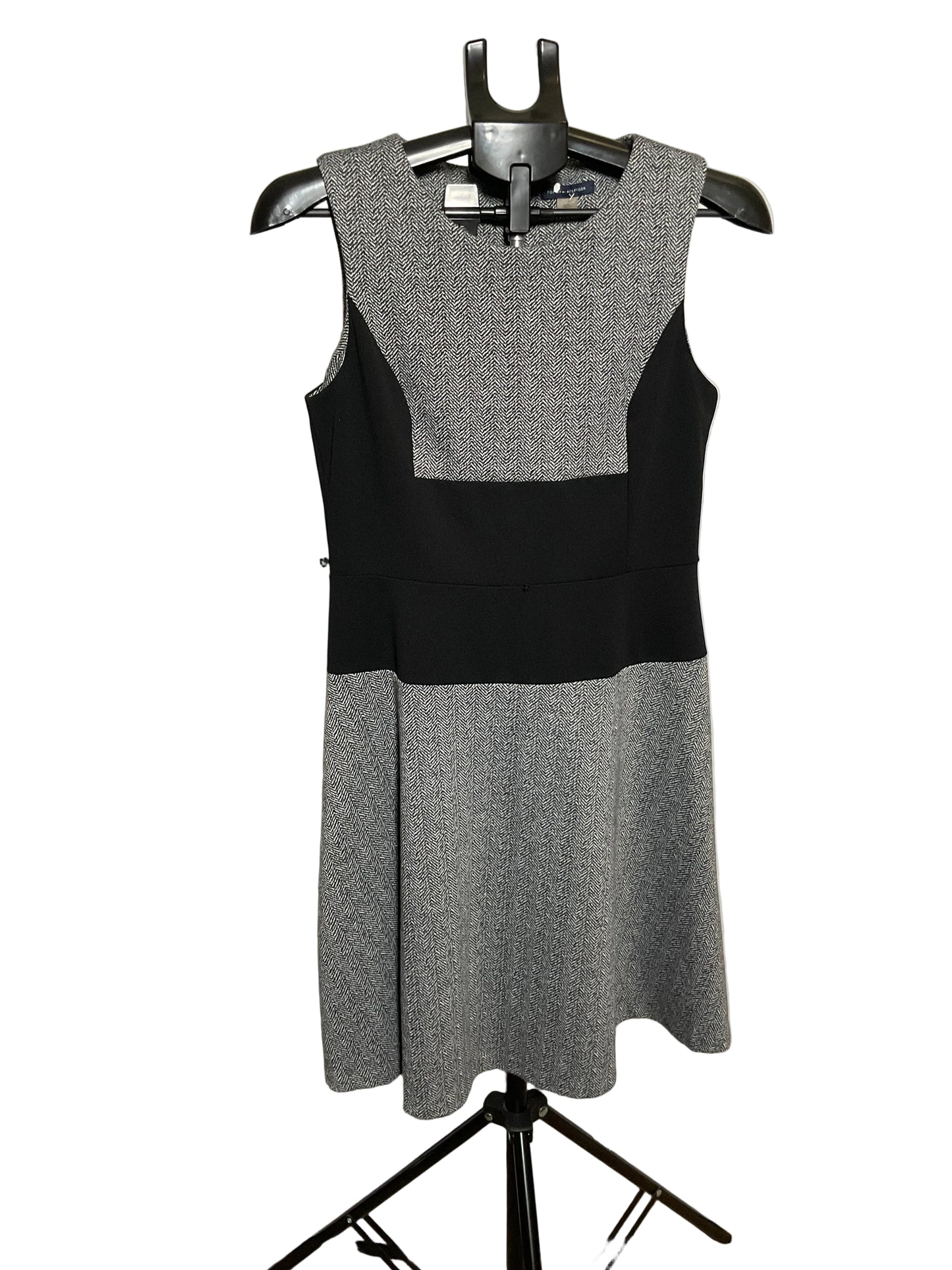 A sleeveless color-block dress on a black hanger, featuring a textured gray yoke and skirt with a solid black waistband, displayed against a white circular studio backdrop.