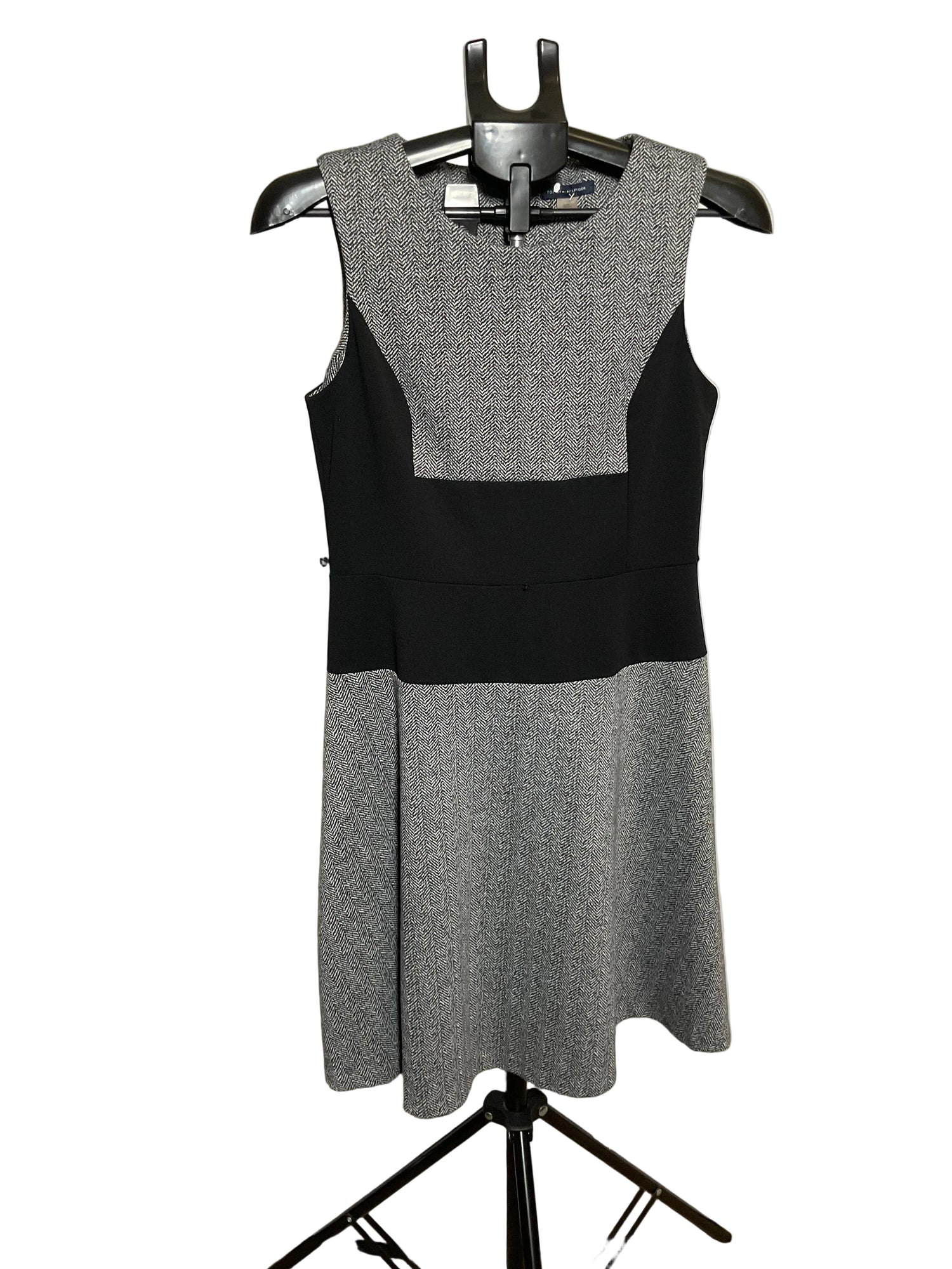 A sleeveless color-block dress on a black hanger, featuring a textured gray yoke and skirt with a solid black waistband, displayed against a white circular studio backdrop.