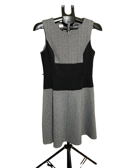 A sleeveless color-block dress on a black hanger, featuring a textured gray yoke and skirt with a solid black waistband, displayed against a white circular studio backdrop.