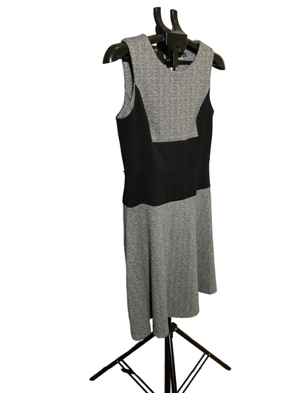A sleeveless color-block knit dress in gray and black, displayed on a black hanger stand in front of a white circular studio backdrop.