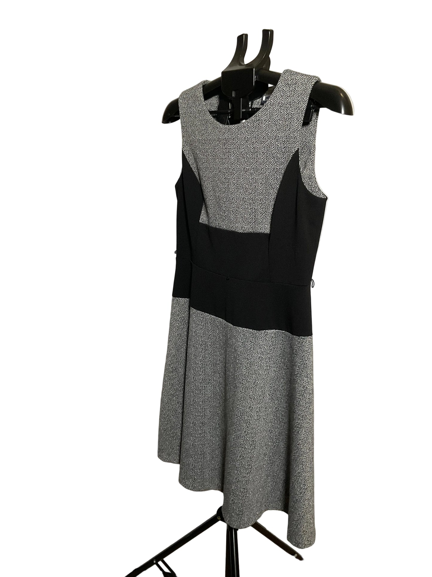 A sleeveless color-block knit dress displayed on a black dress form mannequin. The dress features a heather gray and black color-blocked design, photographed against a white circular studio backdrop.