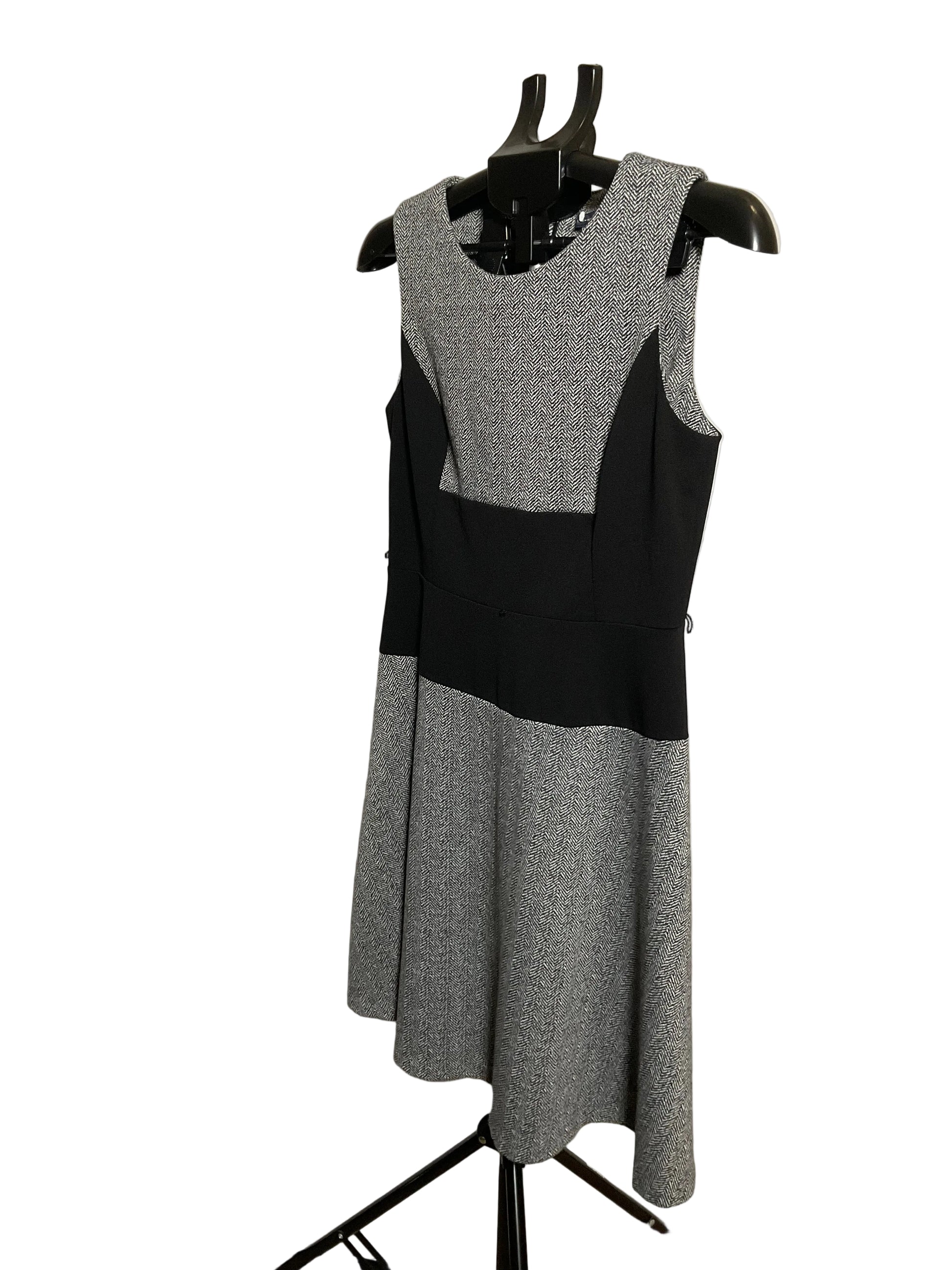 A sleeveless color-block knit dress displayed on a black dress form mannequin. The dress features a heather gray and black color-blocked design, photographed against a white circular studio backdrop.